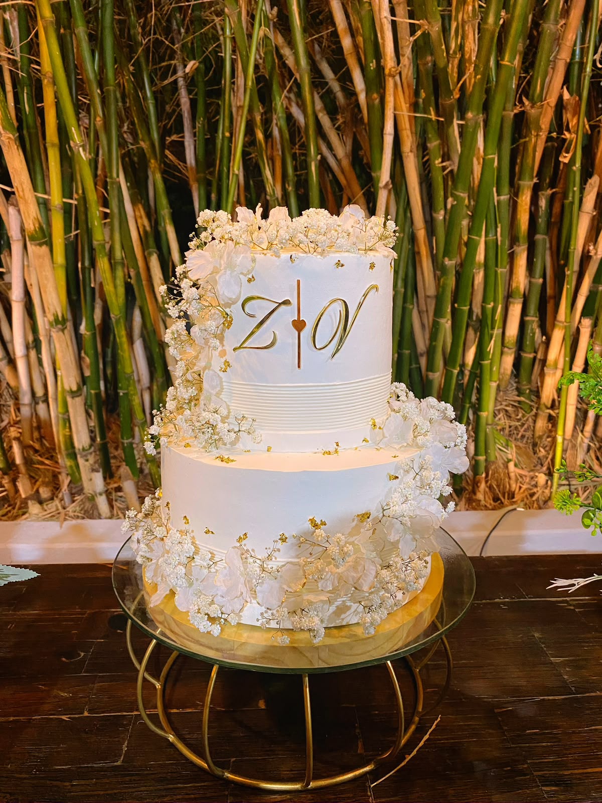 Bolo de casamento branco de dois andares com monograma dourado do casal e flores brancas